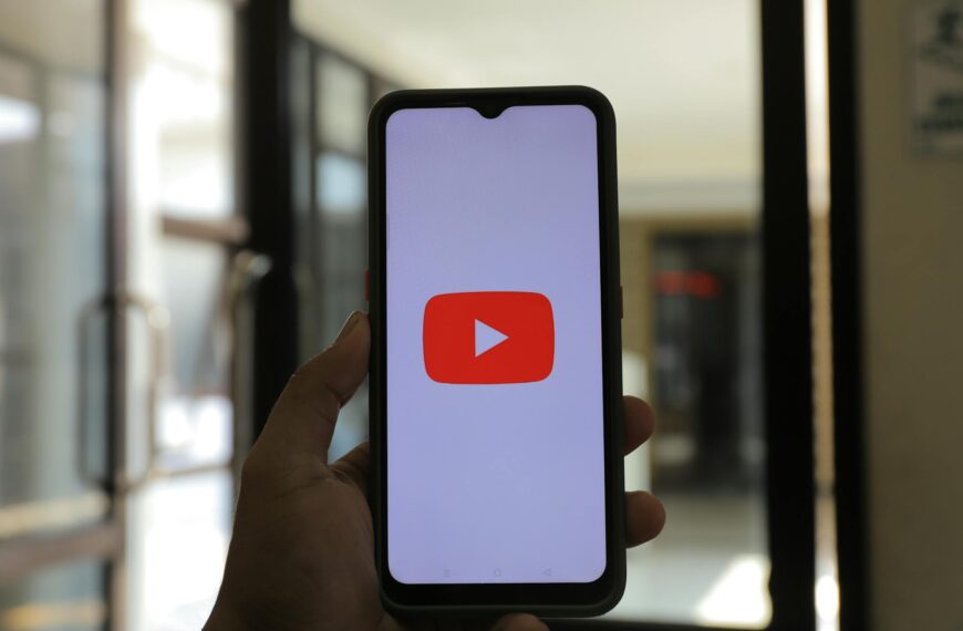 A hand holding a smartphone displaying the YouTube app indoors.