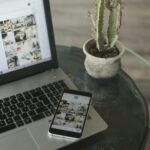 A laptop and smartphone displaying social media apps next to a cactus on a glass table.