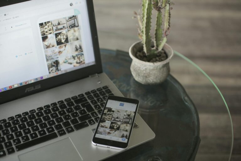 A laptop and smartphone displaying social media apps next to a cactus on a glass table.