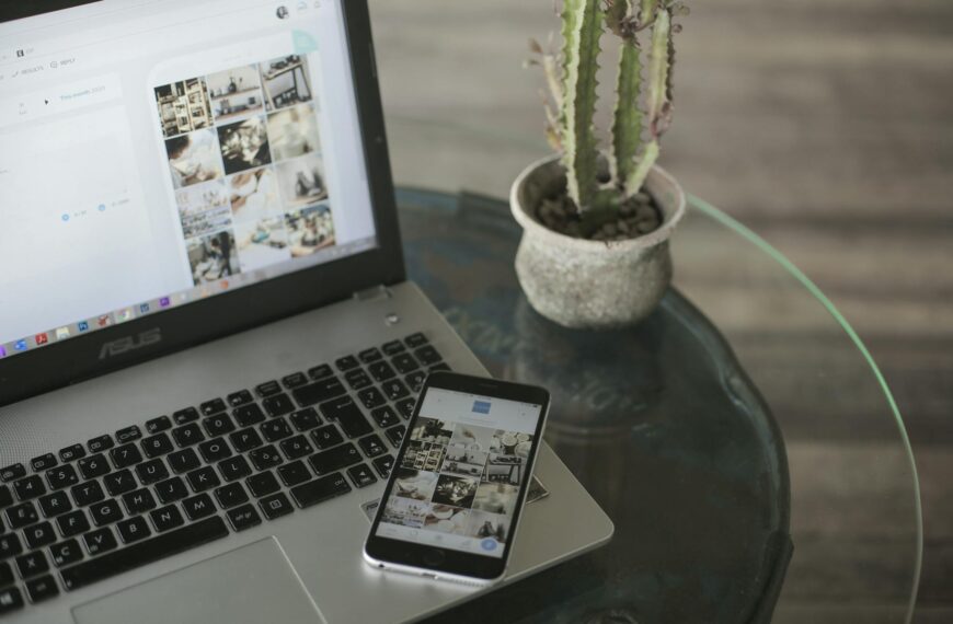 A laptop and smartphone displaying social media apps next to a cactus on a glass table.
