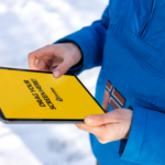 Close-up of hands holding a tablet with a yellow screen in a snowy outdoor setting.